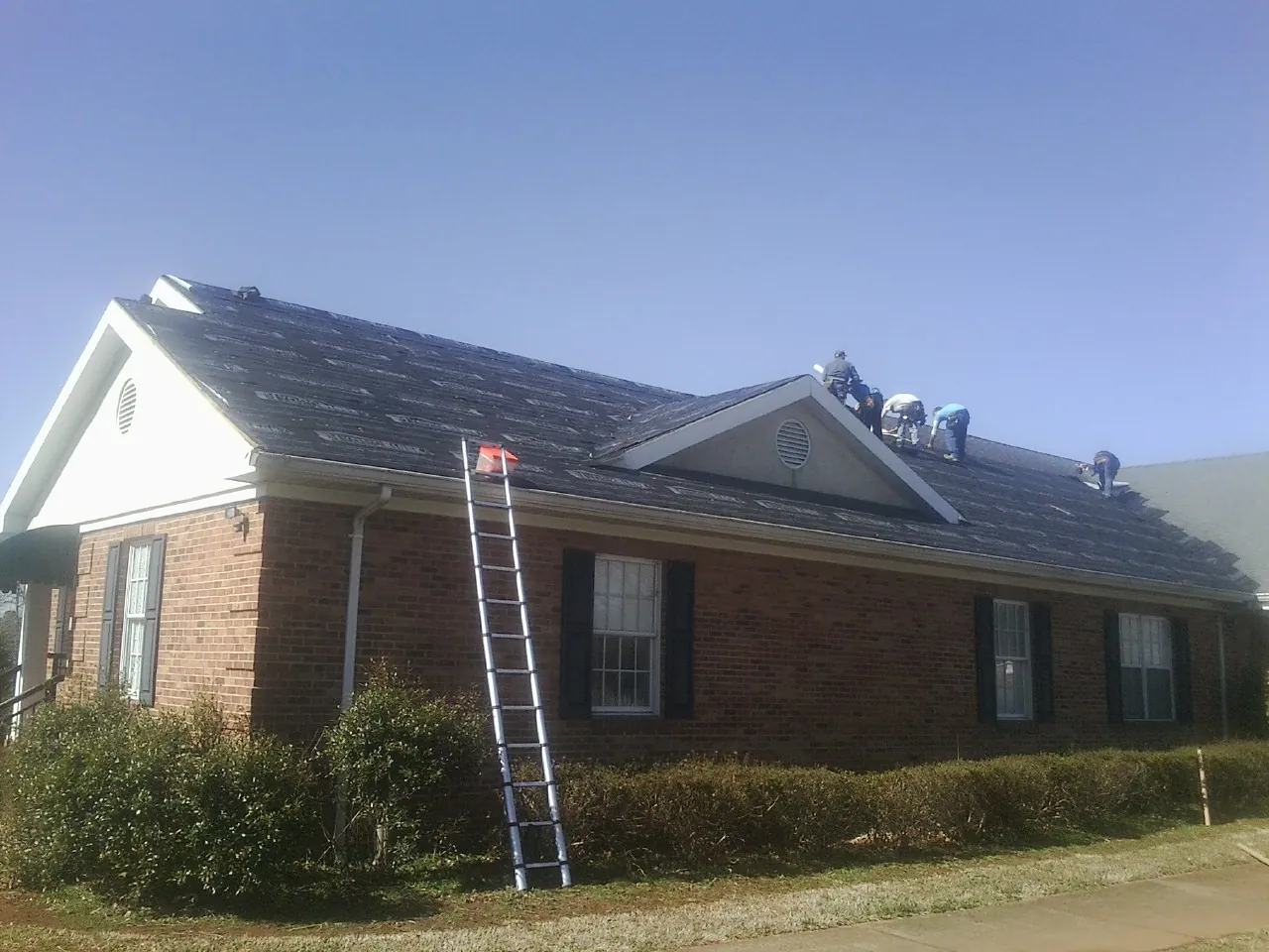 Crew tearing shingles off a brick ranch roof with a ladder set — Metal Roof Repair work by our crew in Sherwood